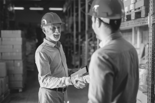 Aging workforce in manufacturing demonstrated by a senior employee shaking hands with a younger person.